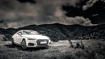 black and white photo of a car on a meadow near the mountains