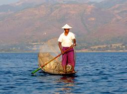 Fisherman in hat, on the boat among the Inle Lake, near the colorful mountains, in Burma