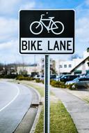 Beautiful landscape with the black and white "Bike Lane" road sign, near the vehicles