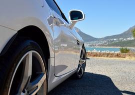 Side view of the beautiful, shiny, white Mercedes car, near the water and mountains