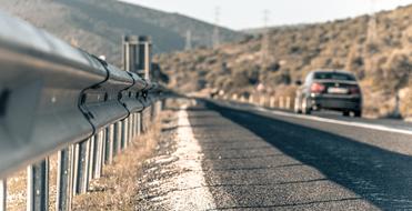 Beautiful landscape of the road with the car, among the colorful mountains and fence, in sunlight