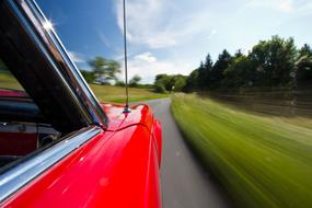 View of the road, among the colorful and beautiful plants, from the shiny, vintage, red and metallic car