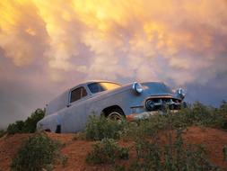 Beautiful landscape with the vintage "Chevrolet" car among the green plants, under the colorful and beautiful clouds at sunset