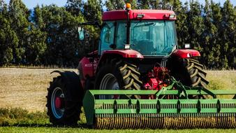 Shiny, red and green tractor on the colorful and beautiful field with plants, near the trees