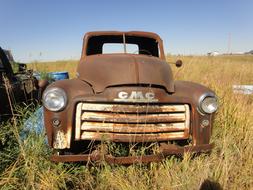 Old, rusty "GMC" truck among the colorful plants on the meadow, in sunlight