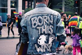 Back view with the man wearing denim jacket with "Born This Way" sign