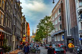 People, vehicles and trees on the colorful street in Amsterdam, Netherlands, under the blue sky with clouds