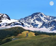 Beautiful, snowy mountains behind the beautiful and colorful mountains with plants, in clouds