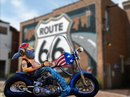 Colorful figure of the biker, on the motorcycle with USA flag, near the building with Route 66 sign