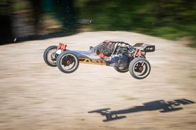 Colorful remote control buggy car in jump, with shadow on the ground, near the plants