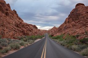 Beautiful landscape of the road, among the colorful rocks and green plants, under the clouds