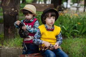 Kids in hats, with the suitcase, on the wet street with plants