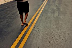 Person in flip-flops, walking on the road with yellow lines