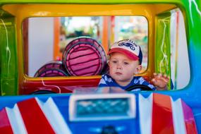 Child boy in cap, in the colorful toy car