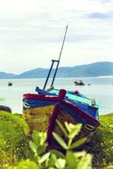 Colorful boat on the beautiful shore with plants, in Vietnam, at background with mountains, under the sky with clouds