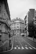 Black and white photo of the beautiful street of Paris, France, with the road among the buildings