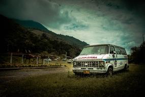 Bus on the grass near the road, near the mountains, under the clouds, in dark frame