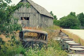 abandoned car in the grass near a wooden barn