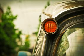 Close-up of the blinker of the shiny "Citroen DS' car, near the green plants