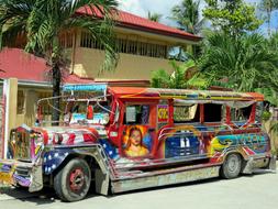 Colorful Jeepney bus with paintings, on the street in Filipino, near the building and green plants