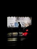 Silhouette of a person in hood, near the building with lights, at the night