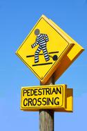 Yellow and black pedestrian crossing sign with white and black model of a person, at blue sky on background