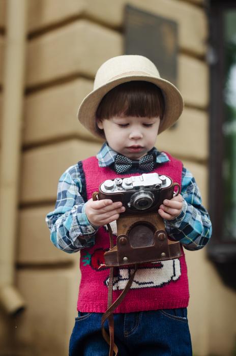 Cute child in hat, with the camera, near the building, on the street, in the rain