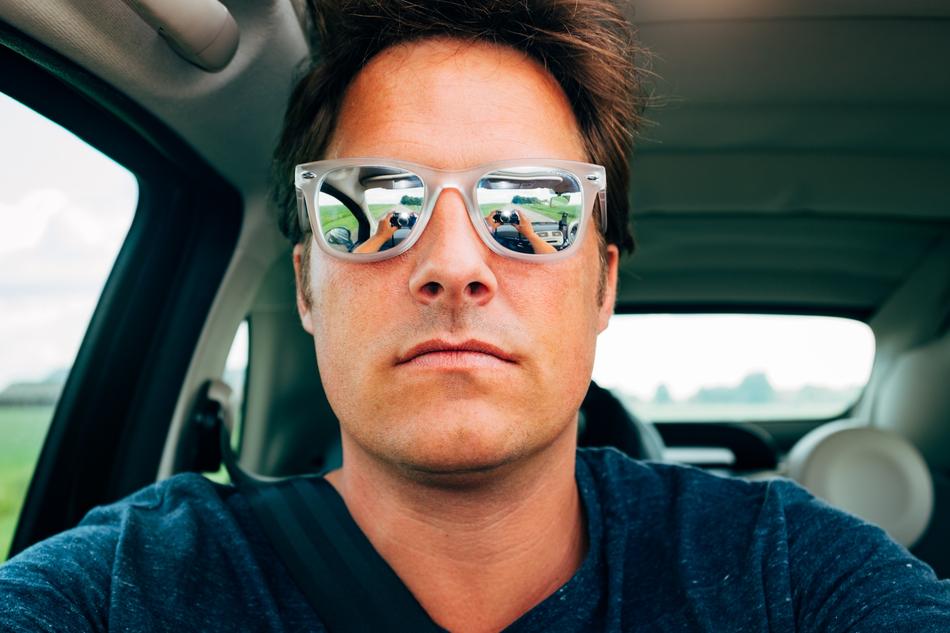 Portrait of the man in shiny sunglasses, in the car, among the green plants