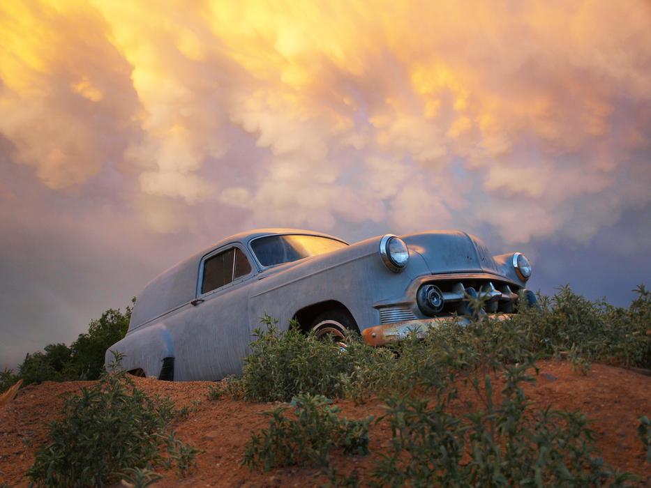 Beautiful landscape with the vintage 'Chevrolet' car among the green plants, under the colorful and beautiful clouds at sunset