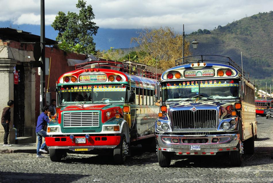People and colorful, shiny busses on the bus station in Antigua Guatemala, near the mountains