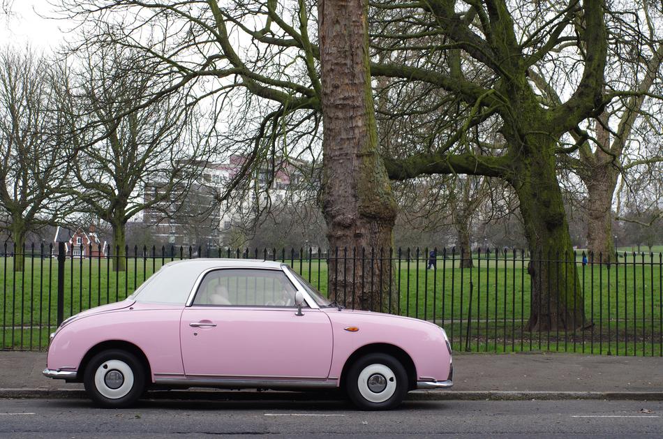 Beautiful landscape with the vintage, pink and white car on the road, near the park with green grass, trees and fence, in London, England