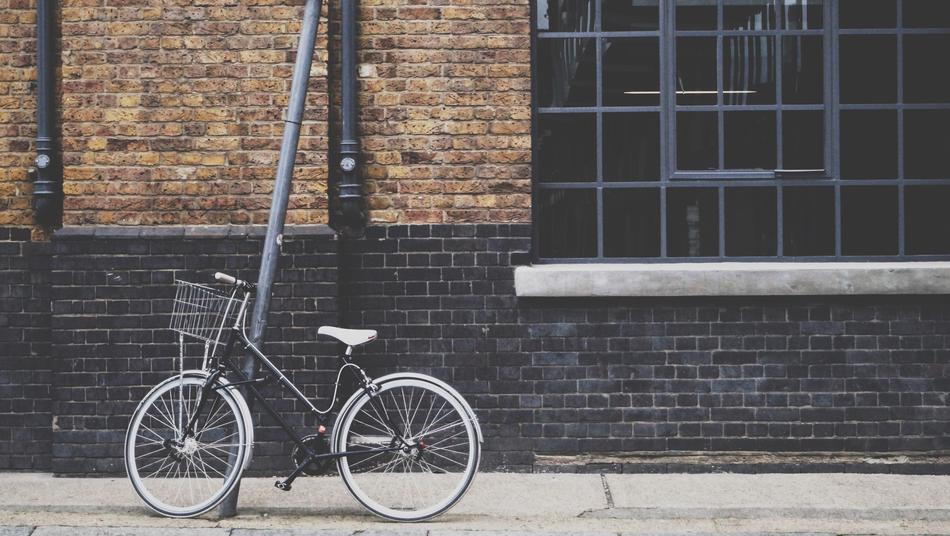 Grey and black bike leaning on the post, near the building with windows