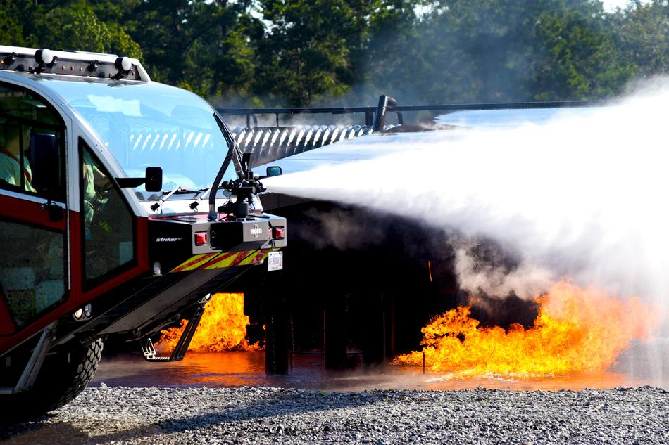Close-up of the fire engine with water, near the fire, at background with trees