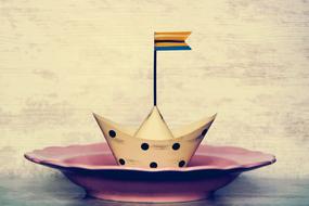 Beautiful, white and black paper ship with the colorful flag, on the red plate