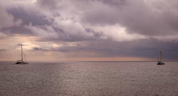 two sailing boats at sea on a background of dark purple sunset