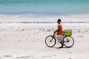 Cyclist, on the sandy beach in Kenya, Africa, near the turquoise water