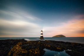 Beautiful landscape with the lighthouse on the shore, at colorful, gradient sunset in the sky, in the evening