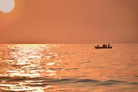 Silhouette of the boat with people, on the beautiful waterscape with ripple, in colorful sunrie