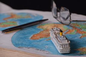 Model of the cruise ship, pen and glasses on the colorful World map