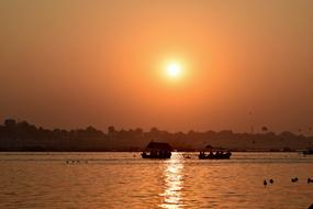 two fishing boats and a flock of ducks swim in the sea against a golden sunset