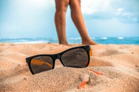 sunglassesand human legs on sand Beach in view of sea