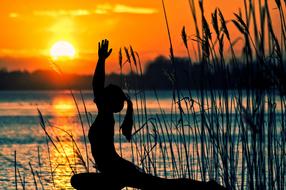 silhouette of a girl in a yoga pose near the water at sunset