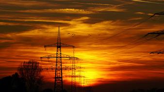 silhouettes of electric towers in the rays of orange sunset