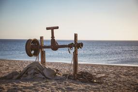 Boat winch on the beautiful sandy beach, near the sea with ripple, at colorful sunset