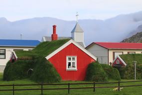 red house with green lawn on the roof against the backdrop of mountains, iceland