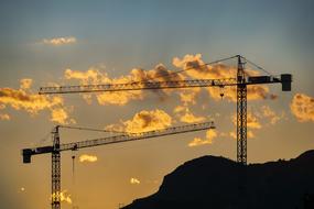 construction cranes on a background of orange clouds and the evening sky