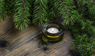 Beautiful, burning candle, near the green fir tree, on the wooden surface on Christmas