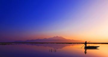 Person on the boat, on the beautiful waterscape, near the mountain, at colorful, gradient sunset, in Turkey