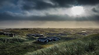 Beautiful landscape of the country houses on the colorful dunes, under the cloudy sky with light, in Denmark