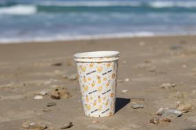 Close-up of the colorful, patterned paper cups, among the colorful seashells on the beautiful, sandy beach of the sea